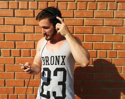 Hipster im Hemd hlt hochwertiges Handy mit Headphone hoch. (Bild: Pixabay)